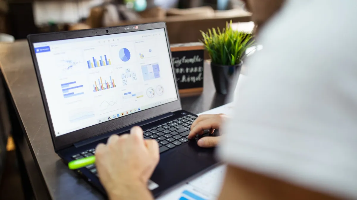 A laptop on a desk showing a financial dashboard of bar and donut charts