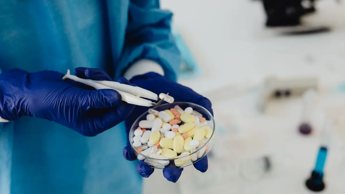 A researcher in gloves handling tablets with tweezers at a laboratory bench