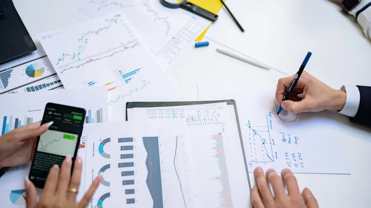 Hands comparing printed financial charts and figures across a desk